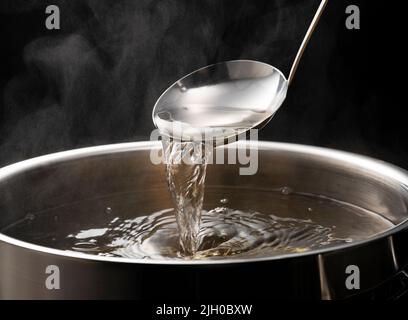 Dashi, Suppenbrühe und die Grundlagen der japanischen Küche. Schwarzer Hintergrund. Dampf. Aushöhlung mit einer Schöpfkelle. Stockfoto