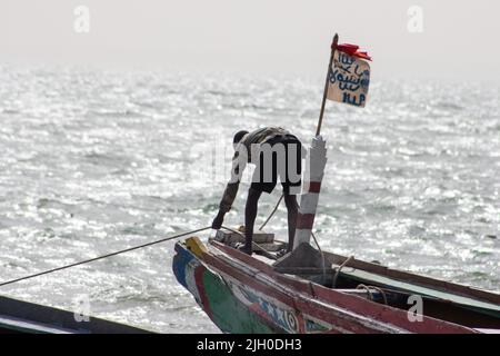 PORTUGIESISCHE STADT, BANJUL, GAMBIA - 10. FEBRUAR 2022 lokales Fischerboot, das schnell mit Flagge geflogen wird Stockfoto