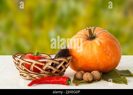 Herbstkomposition mit einem großen Kürbis und Gemüse. Kürbis und Paprika, Aubergine im Weidenkorb, Chili, Walnüsse auf der blu Stockfoto