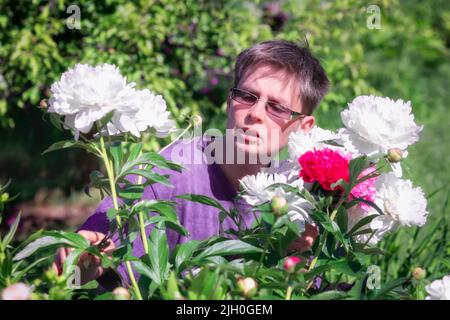 Porträt einer Frau im Garten, die einen Strauß weißer und rosafarbener Pfingstrosen sammelt. Stockfoto