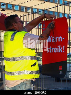 Hamburg, Deutschland. 14.. Juli 2022. Ein Arbeiter legt ein Schild mit der Aufschrift „Warnstreik heute!“ an. An einen Zaun neben einem Eingang zum Container Terminal Burchardkai (CTA) der HHLA (Hamburger Hafen und Logistik AG). Im Konflikt um die Bezahlung von Hafenarbeitern in den großen deutschen Nordseehäfen ist noch keine Einigung in Sicht. Die Gewerkschaft Verdi hat Hafenarbeiter zu einem 48-stündigen Warnstreik aufgefordert. Quelle: Christian Charisius/dpa/Alamy Live News Stockfoto