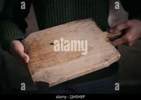 Hoher Winkel der Ernte anonyme Frau in warmen Pullover mit schäbigen Holz Schneidebrett in den Händen Stockfoto