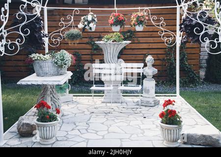 Schmiedeeiserne Stühle neben einem Tisch mit Blumen auf der Terrasse im Sommergarten Stockfoto