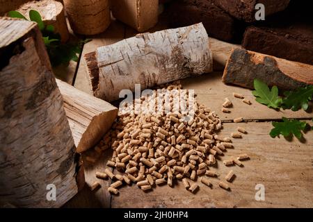 Von oben kleine komprimierte Brennstoff Pellets auf Holztisch in der Nähe gehackte Birken und Eichenstämme und Torfbriketts bei Tageslicht verstreut Stockfoto