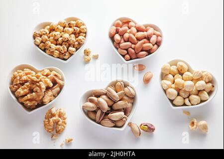 Von oben von verschiedenen Arten von gesunden Nüssen serviert auf Keramik herzförmigen Schalen auf weißem Hintergrund in Licht Studio Stockfoto