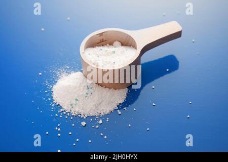 Von oben Stapel von verstreuten weißen Waschmittel in Holz Messbecher auf Metall blauen Hintergrund in Licht Studio platziert Stockfoto