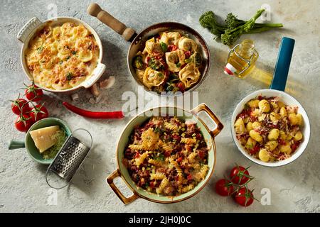 Um leckere Gerichte der italienischen Küche in Pfannen und Aufläufen mit frischen Zutaten auf dem Tisch zu sehen Stockfoto