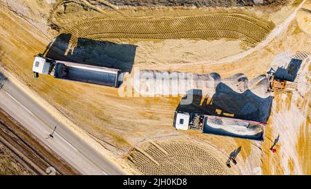 Oben Ansicht, Overhead auf zwei Kipper-Lastwagen als Heben ihren Anhänger, um Ladung zu entladen, Bruch, kleinen zerkleinerten Stein, dass Bulldozer Crawler ist Pushin Stockfoto