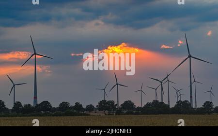 Mallnow, Deutschland. 13.. Juli 2022. Durch eine Wolkenlücke über der Landschaft mit Windturbinen scheint der farbenfrohe Sonnenuntergang. Quelle: Patrick Pleul/dpa/Alamy Live News Stockfoto