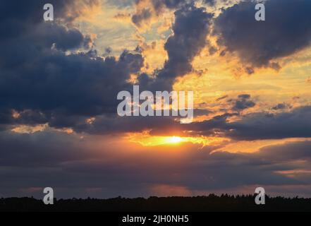 Sieversdorf, Deutschland. 13.. Juli 2022. Der Sonnenuntergang scheint bunt durch eine Wolkenlücke über der Landschaft in Ostbrandenburg. Meteorologen sagen auch viel Sonnenschein für die kommenden Tage voraus. Quelle: Patrick Pleul/dpa/Alamy Live News Stockfoto