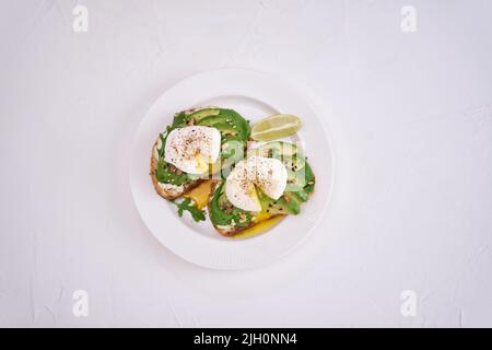 Frisch gebackene pochierte Eier und Avocado-Toasts auf hellgrauem Hintergrund Stockfoto