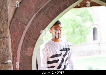 Junger indischer Mann posiert neben einem historischen Steinfenster im Lodhi Garden in Neu-Delhi. Stockfoto