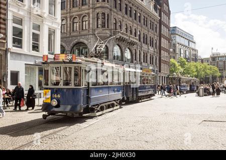 Oldtimer-Straßenbahnen, die auf einem belebten Dam-Platz in Amsterdam, Niederlande, geparkt wurden. Stockfoto