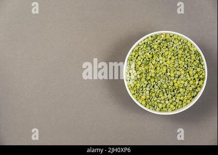 Ungekochte Speisen. Zerteilte Erbsen in einer weißen Keramikschale trocknen. Grüne Bohnen. Grauer Hintergrund. Draufsicht. Platz für Text- und Designelemente kopieren Stockfoto