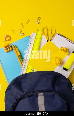 Vertikales Video der Komposition mit Rucksack und Schulsachen auf gelber Oberfläche Stockfoto