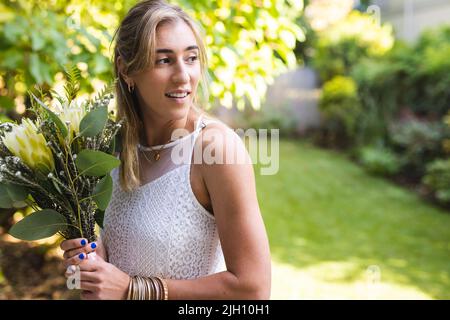 Bild von glücklichen kaukasischen Frau im Hochzeitskleid mit Blumen Stockfoto