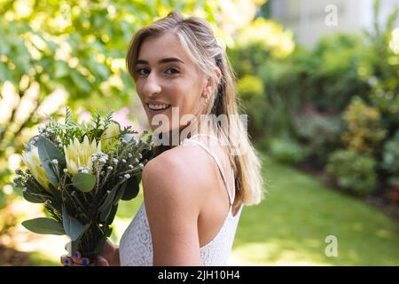 Bild von glücklichen kaukasischen Frau im Hochzeitskleid mit Blumen Stockfoto