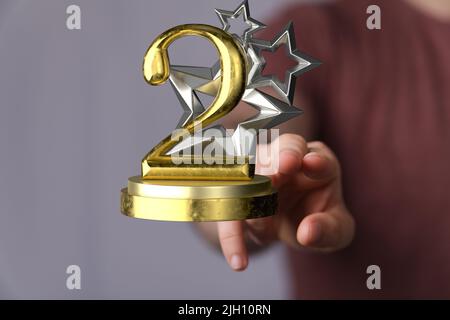 Eine 3D Rendering eines zweiten Platz goldenen Auszeichnung eine männliche Hand hält auf einem verschwommenen Hintergrund Stockfoto
