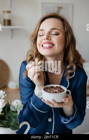 Schönes Mädchen in Pyjamas essen Getreide in der Küche Stockfoto