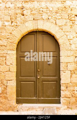 Die Fassade eines alten Steinhauses mit einer Holztür auf der Mittelmeerinsel Rhodos Stockfoto