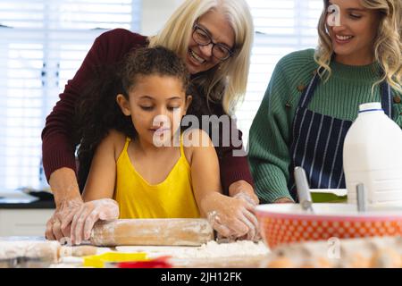 Multirassische mehrgenerationenweibliche Familie Knetteig mit Nudelholz auf dem Tisch in der Küche Stockfoto