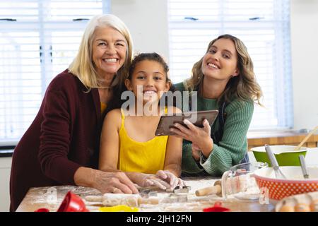 Porträt einer glücklichen multirassischen, mehrgenerationenigen Familie mit digitalem pc, der das Essen auf dem Tisch zubereitete Stockfoto