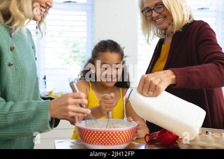 Glückliche multirassische mehrgenerationenfähige weibliche Familie, die in der Küche Backwaren auf dem Tisch zubereitet Stockfoto