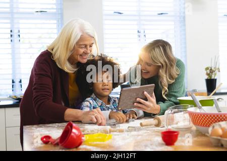 Fröhliche multirassische Mutter und Großmutter zeigen Rezept für Jungen über digitalen pc in der Küche Stockfoto