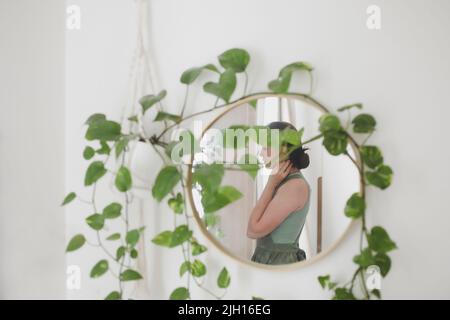 Junge Frau im Vorfeld, Hausfrau oder Gärtner kümmert sich um grüne Pflanze, Bewässerung Blumentöpfe in gemütlichen Raum. Konzept der Gartenarbeit und Hobby Stockfoto