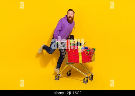 Foto in voller Größe von aufgeregt überglücklich Person springen voll Warenkorb Geschenke auf gelbem Hintergrund isoliert Stockfoto