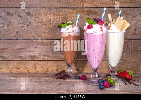 Sommerliche Erfrischungsgetränke, Milchshakes, verrückte Shakes mit Eis, Beeren, Vanille, Schokolade. Auf klassischem Holzhintergrund Stockfoto