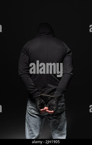 Rückansicht eines afroamerikanischen Banditen in Kapuzenpullover und Handschellen, die isoliert auf Schwarz stehen Stockfoto