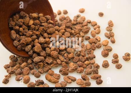 Nahaufnahme eines Bündels getrockneter Tandernüsse (cyperus esculentus), verstreut auf einem weißen Tisch mit Platz zum Kopieren Stockfoto