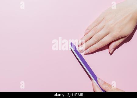 Frau Feilen ihre Nägel mit lila Fimger-Datei, machen Maniküre zu Hause, Handpflege, Zeit für sich selbst Konzept. Rosa Hintergrund. Draufsicht. Stockfoto