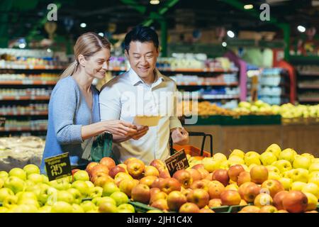 Glücklich gemischte Rennen asiatische Paar Familie Mann und Frau Wahl Obst oder Gemüse im Supermarkt. Gemeinsames tägliches Shoppen. Käufer Kunde wählen Produkt Pick einen Apfel in Öko-Beutel Stockfoto