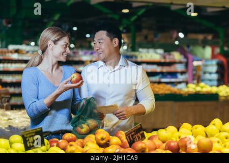 Glücklich gemischte Rennen asiatische Paar Familie Mann und Frau Wahl Obst oder Gemüse im Supermarkt. Gemeinsames tägliches Shoppen. Käufer Kunde wählen Produkt Pick einen Apfel in Öko-Beutel Stockfoto