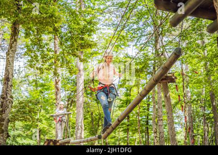 Glückliche Frauen Mädchen weiblich Gleiten Klettern in extremen Straße Trolley Zipline im Wald auf Karabiner Sicherheitslink auf Baum zu Baum top Seil Abenteuerpark Stockfoto