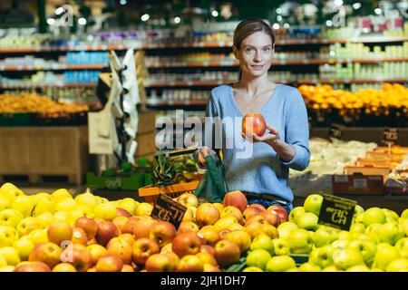 Frau wählt Obst Gemüse auf der Theke im Supermarkt. Weibliche Hausfrau einkaufen auf dem Markt in der Nähe von Gemüse Kaufhaus mit einem Korb in den Händen. Untersucht Apfel Stockfoto