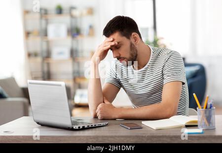 Gestresster Mann mit Laptop, der im Heimbüro arbeitet Stockfoto