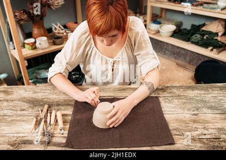 Kunstvoll auf Tontopf geschnitzt, Töpferei Prozess. Junge talentierte Künstler dekorieren Glas im Studio Interieur Stockfoto