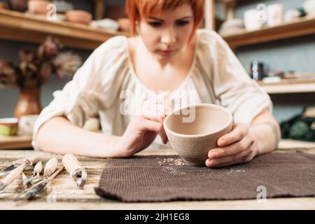 Tonschüssel Dekoration, Schnitzerei auf Keramik. Junge Handwerkerin beendet ihre Kreation im Studio Stockfoto