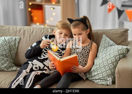 Kinder in halloween Kostümen lesen Buch zu Hause Stockfoto