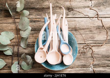 Tonlöffel in Tonschüssel flach legen. Nahaufnahme von vielen Tonlöffeln in Tonschüssel auf Holzhintergrund. Handgemachte dekorative Tonlöffel in Tonschale. Stockfoto