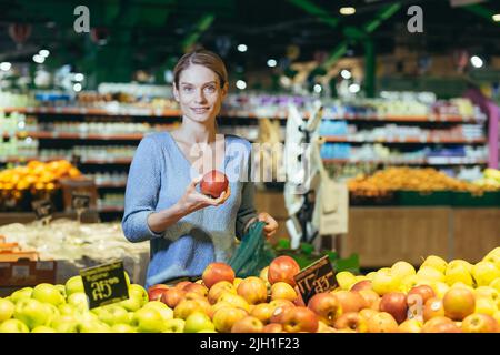 Frau wählt Obst Gemüse auf der Theke im Supermarkt. Weibliche Hausfrau einkaufen auf dem Markt in der Nähe von Gemüse Kaufhaus mit einem Korb in den Händen. Untersucht Apfel Stockfoto