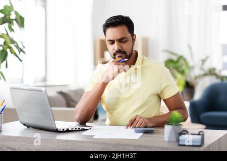 Mann mit Rechner und Papier, der zu Hause arbeitet Stockfoto