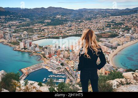 Rückansicht Frau auf dem Gipfel des Penon de Ifach-Felsens Genießen Sie eine malerische Aussicht auf das Meer, die Berge und die Stadtlandschaft. Wahrzeichen, Wanderkonzept. Calpe Spanien Stockfoto