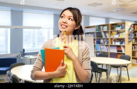 asiatische Studentin mit Büchern in der Bibliothek Stockfoto