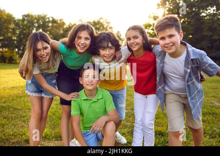 Ein Haufen fröhlicher kleiner Freunde umarmt sich und posiert für ein Gruppenfoto im Park Stockfoto