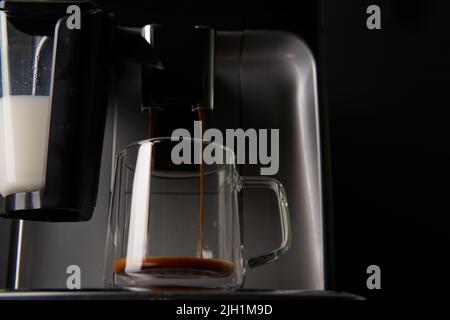 Frisch gebrühter Kaffee wird aus der Kaffeemaschine in Glasbecher gegossen. Professionelles Brühen von Kaffee zu Hause. Stockfoto