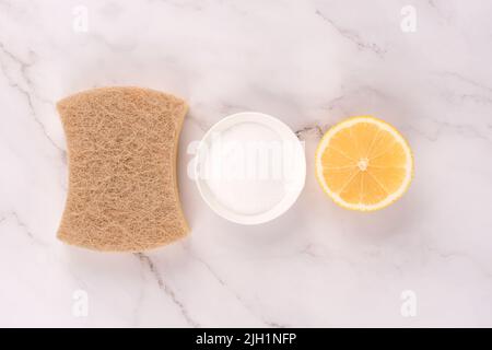 Natürliches Haushaltsreinigungsbündel mit Öko-Zutaten - Nussbaum-Geschirrtuch, Zitrone, Backpulver oder Zitronensäure über Marmor Arbeitsplatte Tischhintergrund. Stockfoto